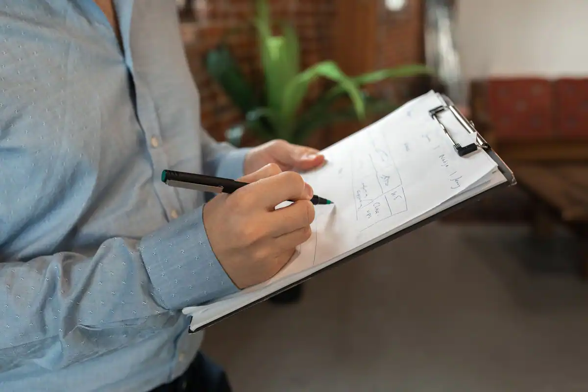 Persoană care bifează pe un clipboard lista actelor pentru vânzarea apartamentului