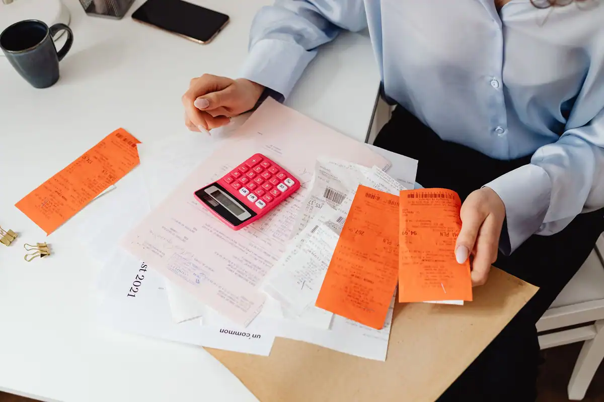 Femeie care adună chitanțe și facturi cu un calculator roz, evaluând datoriile moștenirii
