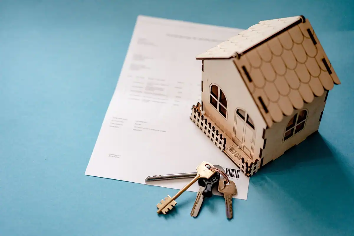 Machetă de casă din lemn și chei pe un document de transfer al proprietății