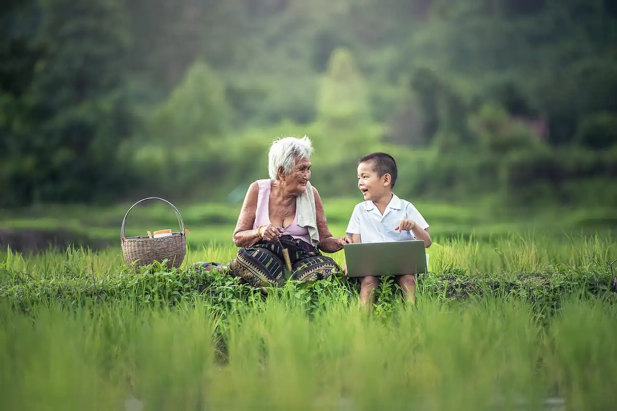Bunică și nepot zâmbitori stând în iarbă, două generații ale aceleiași familii