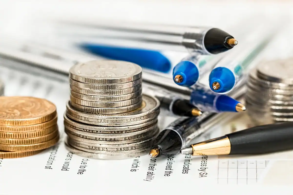 Teancuri de monede și pixuri pe o foaie, pentru calculul onorariului notarial