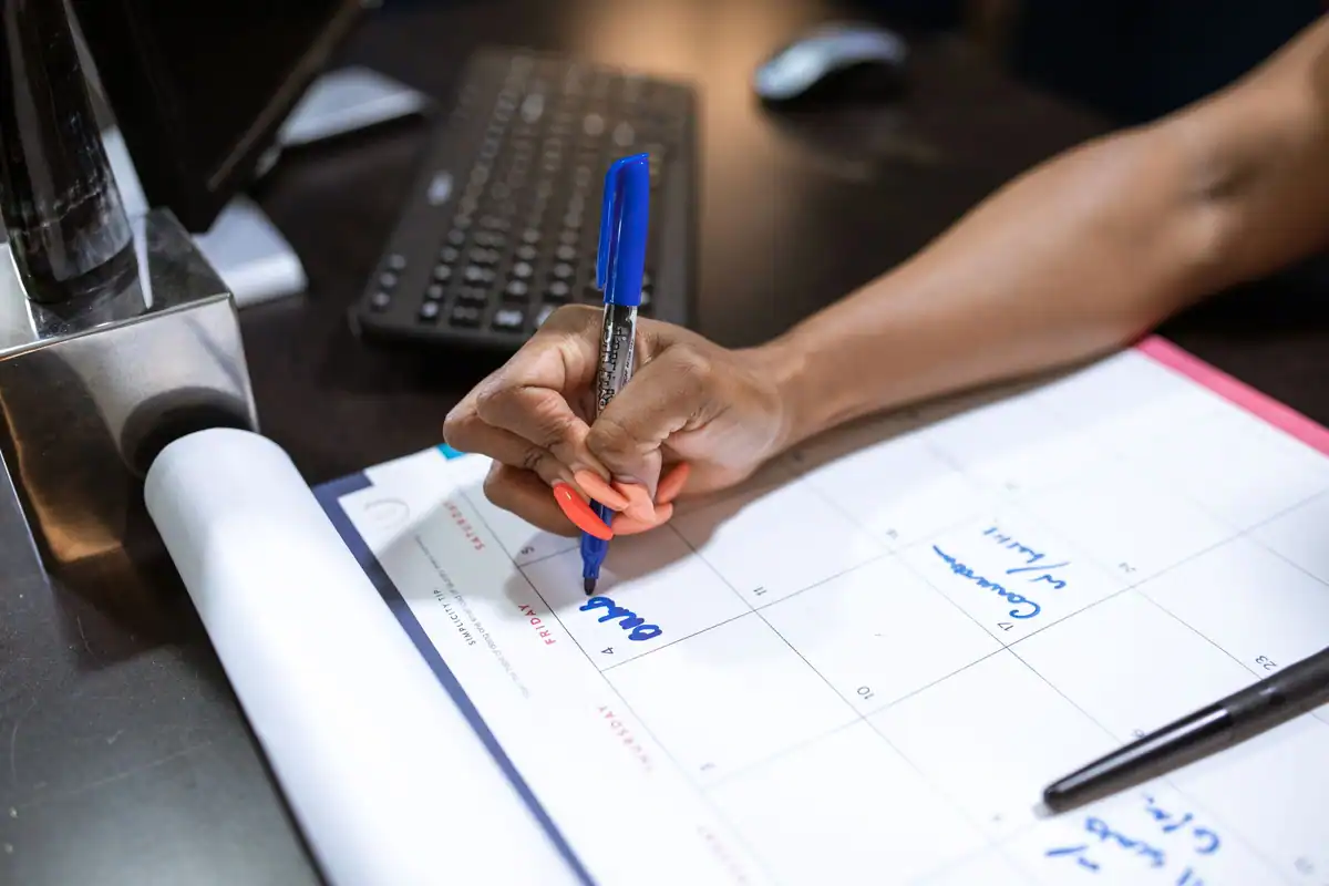 Mână care notează data programării la notar într-un calendar cu marker albastru