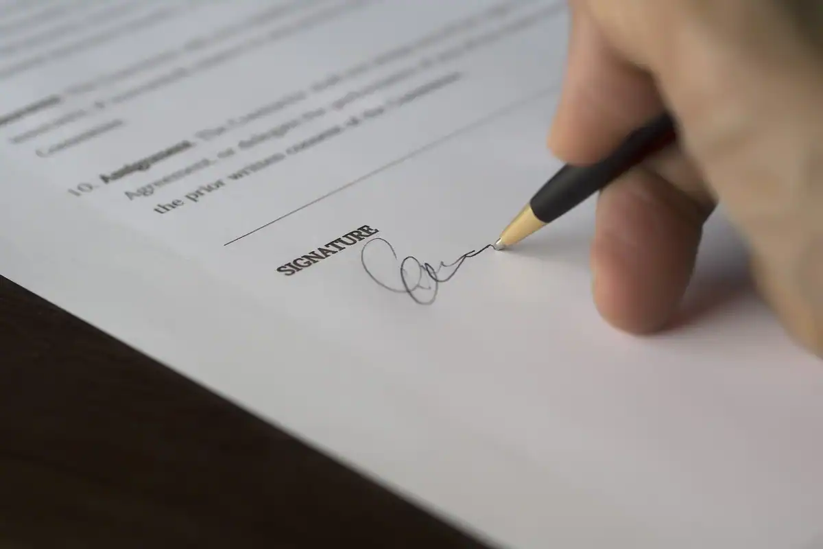 Mână care semnează pe rândul de semnătură al unui document tipărit