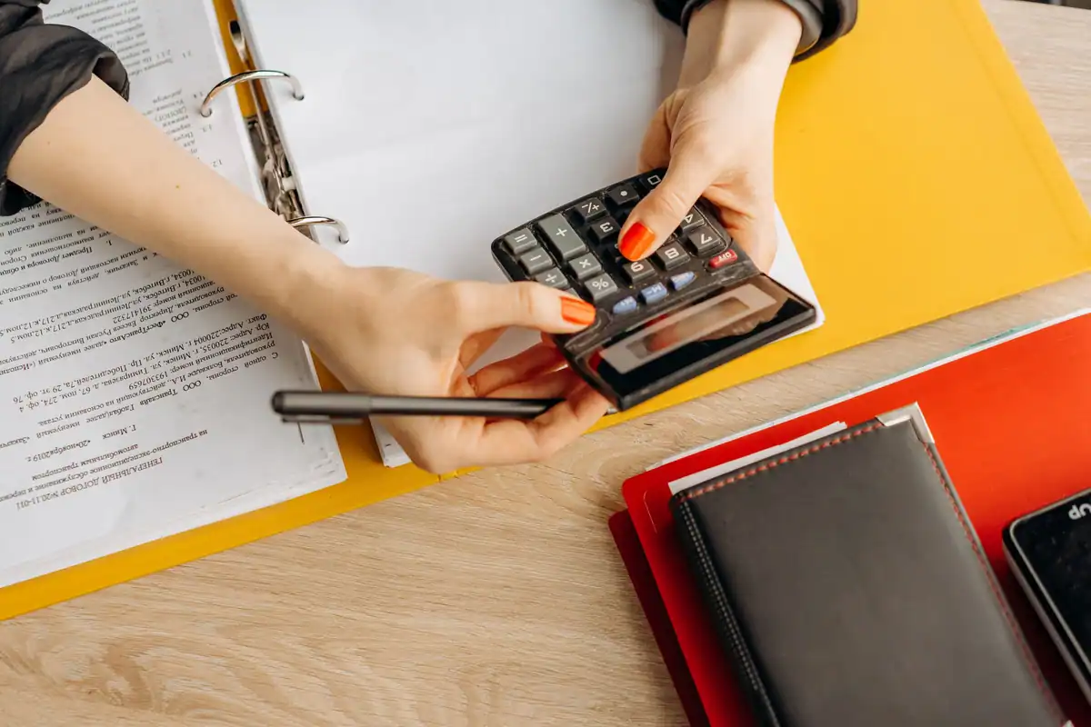 Mâini care folosesc un calculator lângă un biblioraft cu documente