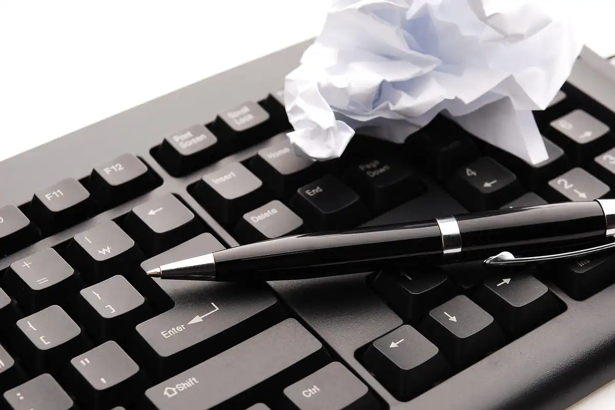 Hârtie mototolită și stilou pe o tastatură, simbol al renunțării la un act