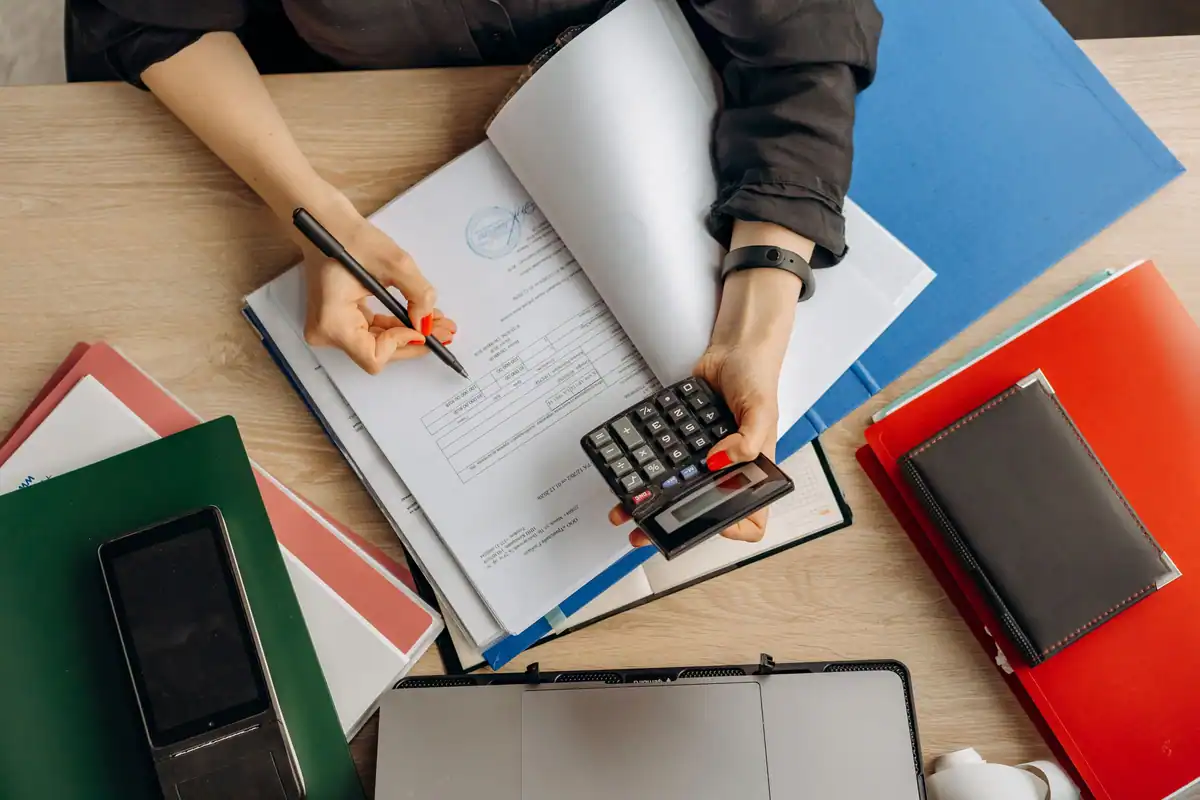Persoană care face calcule cu un calculator printre dosare colorate