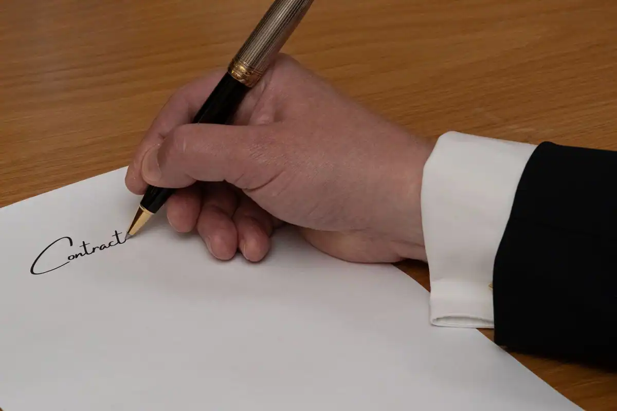 Mână care semnează cu stiloul un document pe un birou de lemn